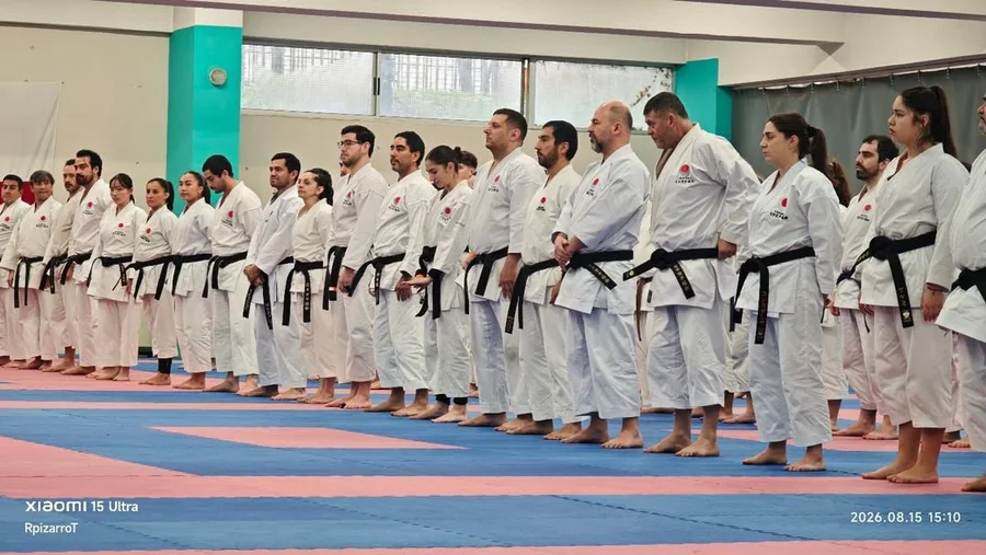 Fila de karatecas con cinturones negros reunidos en un gimnasio.