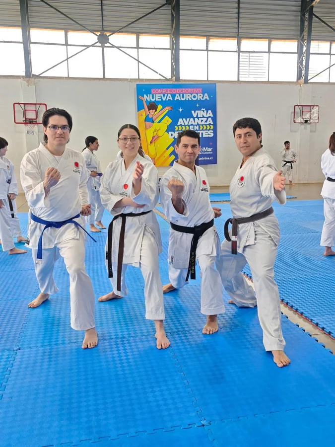 Cuatro practicantes de karate posan en guardia sobre un tatami azul.