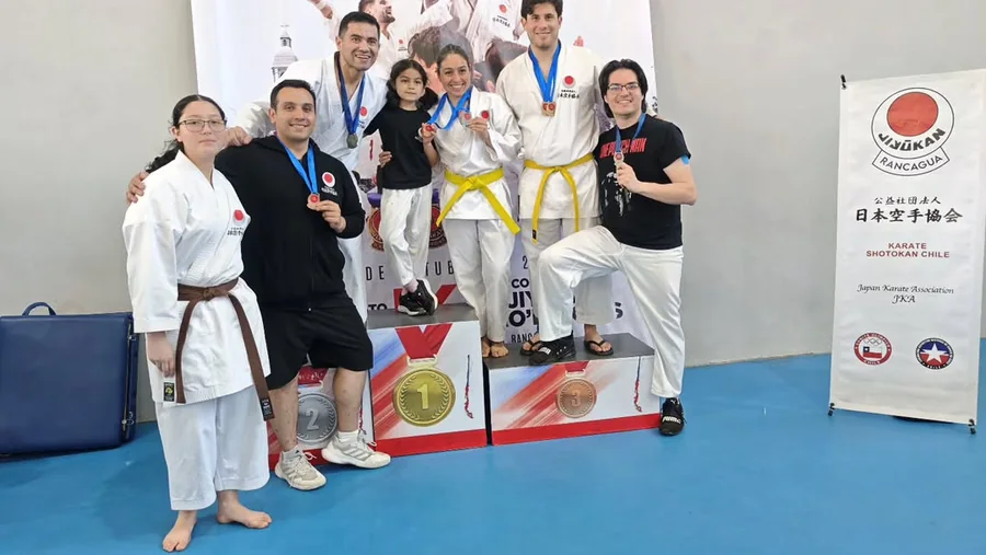 Karatecas posan junto a un podio con medallas y un pendón de JKA Chile.